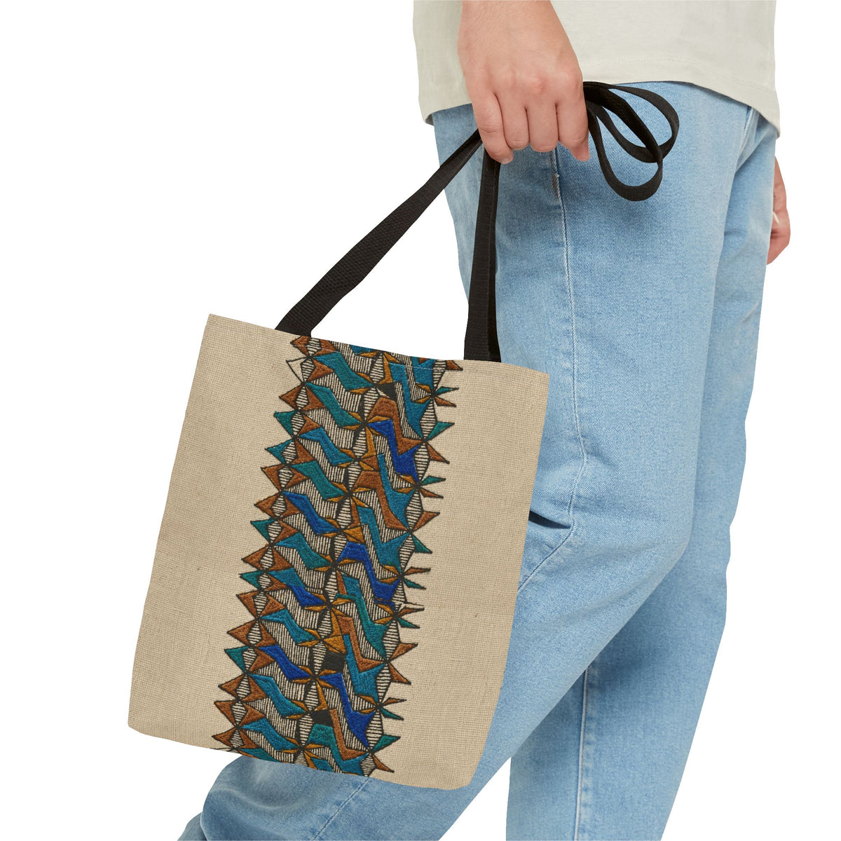 Boho Geometric Everyday Patterned Canvas Tote Bag With Reinforced Handles, 3 Sizes, carried by hand beside casual blue jeans, highlighting its blue and tan print and black shoulder handles. Patterned canvas tote for art tote, beige bag, bohemian bag, boho tote, canvas tote, eco shopping, everyday tote, gift for her, market bag, neutral tote, printed tote, summer tote, and tribal tote use.