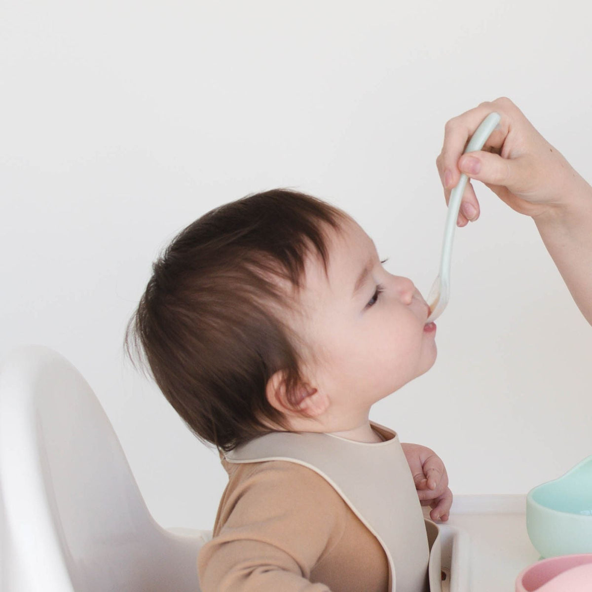 Adult feeding a baby with a flexible spoon from the Bite Size Bundle Baby's Brew toddler feeding set