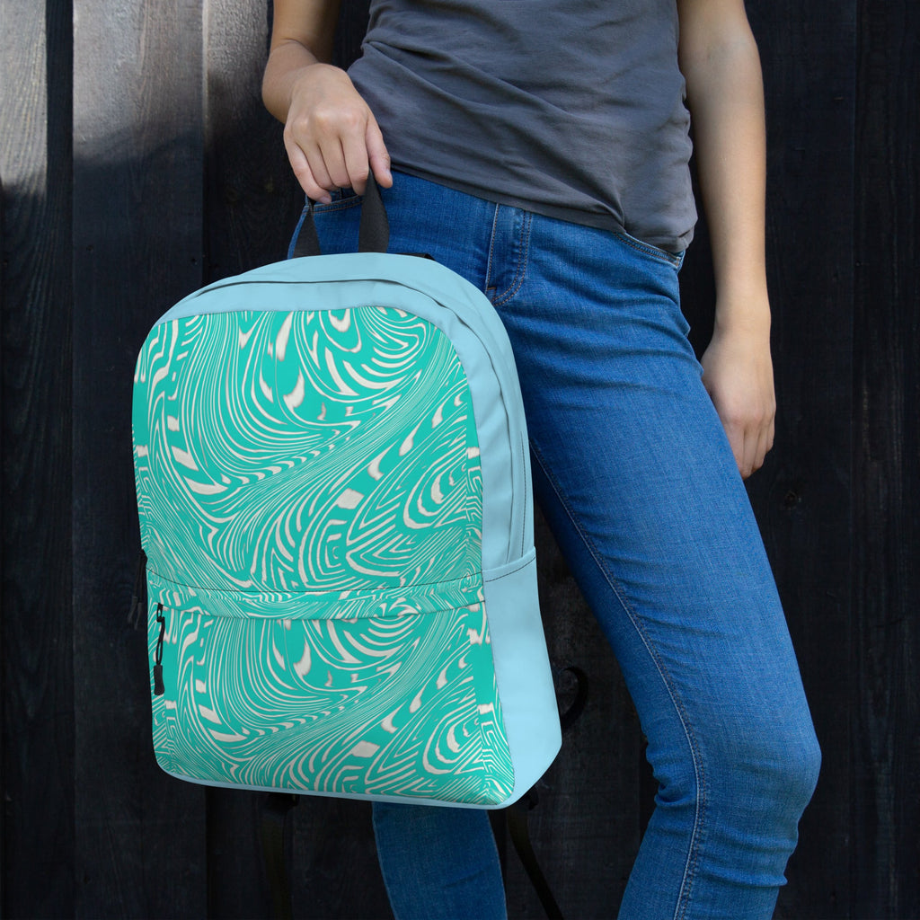 Close-up of a fashionable water-resistant backpack, suitable for back to school use with an apple laptop holder, shown in use by a young woman, featuring a trendy swirl design while resting on her hip.